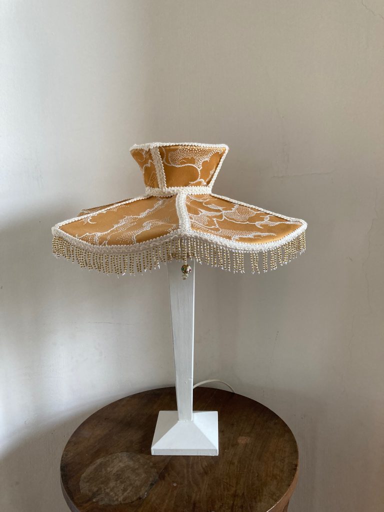 Lampe sur pied avec un abat-jour jaune orné de motifs et de perles, reposant sur une base en bois.